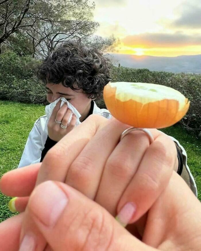 Person holding an orange slice on their finger like a ring with someone in the background wiping tears in a creative pose.