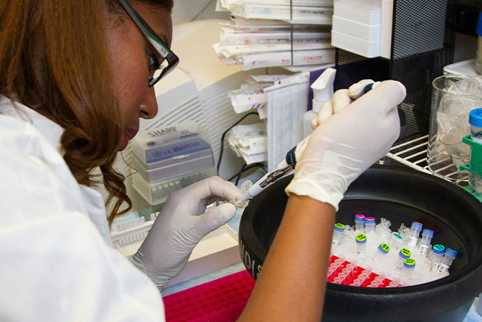 Lab technician in gloves using a pipette in a DNA lab mixing paternity test samples for analysis.