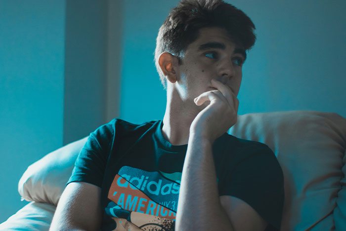 Young man sitting on a couch looking thoughtful, representing DNA lab mixes paternity results and family reconnection.