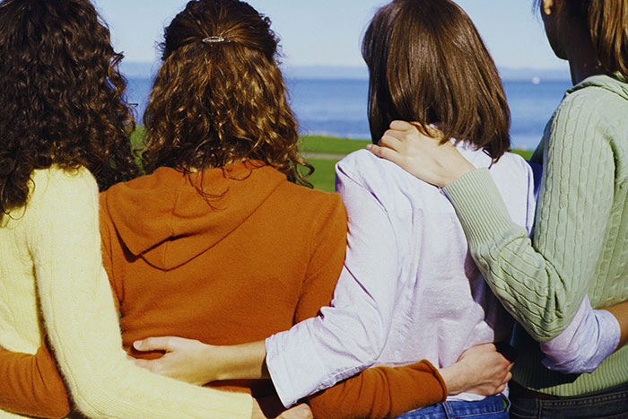 Four women standing side by side outdoors with arms around each other, symbolizing men’s feelings they keep to themselves.