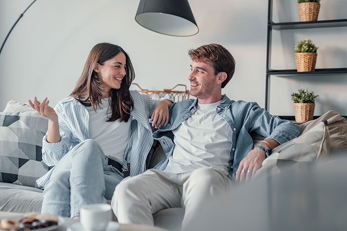 A young couple sitting on a couch having an open conversation about things men keep to themselves in relationships.