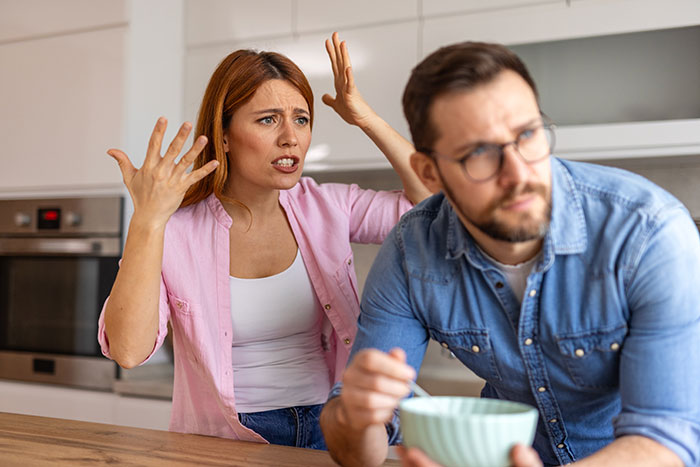 A frustrated woman gesturing while a man eats cereal, illustrating things men keep to themselves in relationships.
