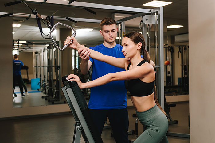 Male personal trainer guiding woman on strength machine, illustrating things men keep to themselves but want to tell women.