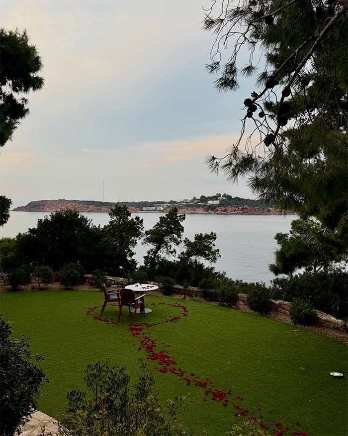 Romantic Greek proposal setup with rose petals and chairs overlooking the sea featuring most beautiful girl in the world.
