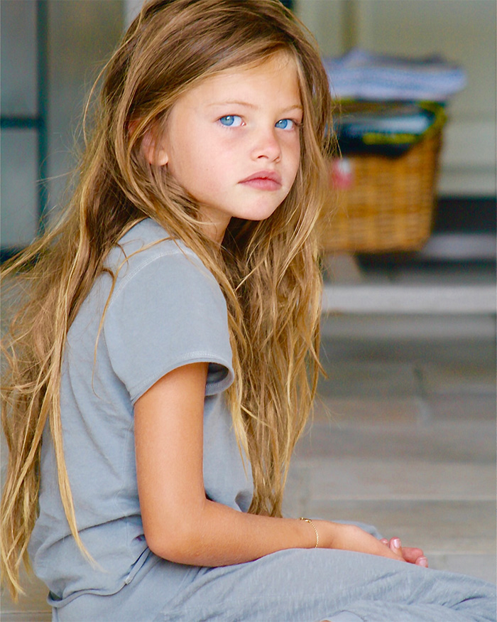 Young girl with long hair and blue eyes sitting indoors, representing the most beautiful girl in the world concept.