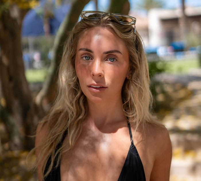 Young woman with blonde hair and sunglasses on her head, posing outdoors with shadows in a natural setting related to Bonnie Blue criminal charge.