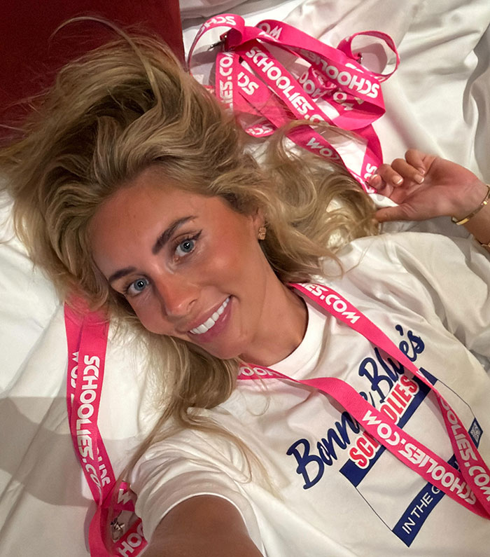Blonde woman wearing Bonnie Blue shirt and pink lanyard, smiling while lying down for a casual selfie.