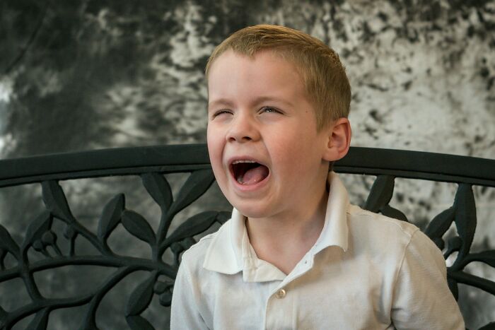 Young boy on decorative bench laughing with mouth wide open, capturing playful and on point comebacks moment.