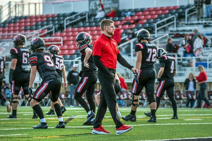 Football coach walking on field while players prepare, illustrating moments when sabotage leads to karma consequences.