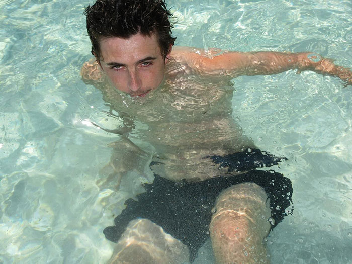 Timothée Chalamet in a pool wearing black swim shorts, captured in a candid moment with water reflections around him. Timothée Chalamet in a pool wearing black swim shorts, captured in a candid moment with water reflections around him.