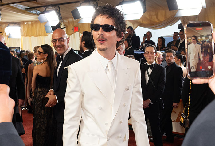 Timoth&eacute;e Chalamet in white suit and sunglasses at a red carpet event amid ballet drama and Sydney Sweeney news.