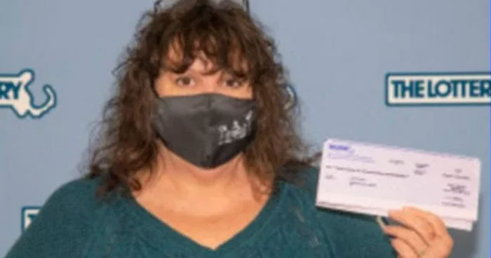 A woman wearing a black mask holds a lottery check, illustrating humans neurologically entering adulthood at age 32.