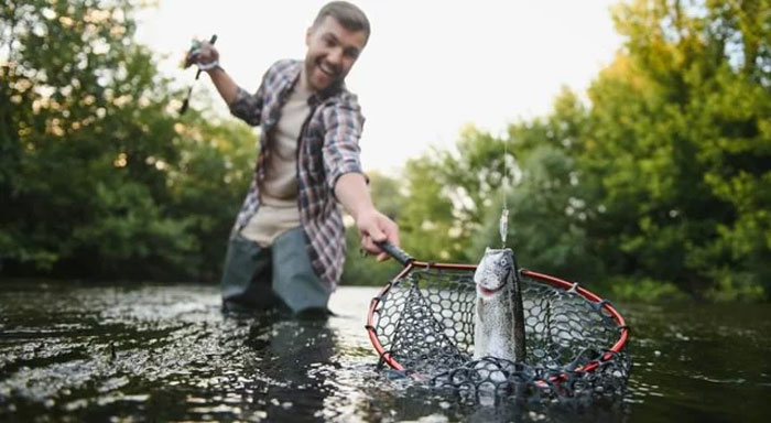 Man fishing in a river holding a net with a caught fish, illustrating humans neurologically enter adulthood at age 32.