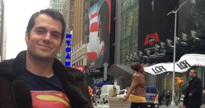 Man wearing Superman shirt and black jacket standing on busy city street with pedestrians and billboards, adulthood concept.