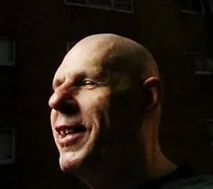 Bald man smiling in low light with focus on face, illustrating humans neurologically entering adulthood at age 32.