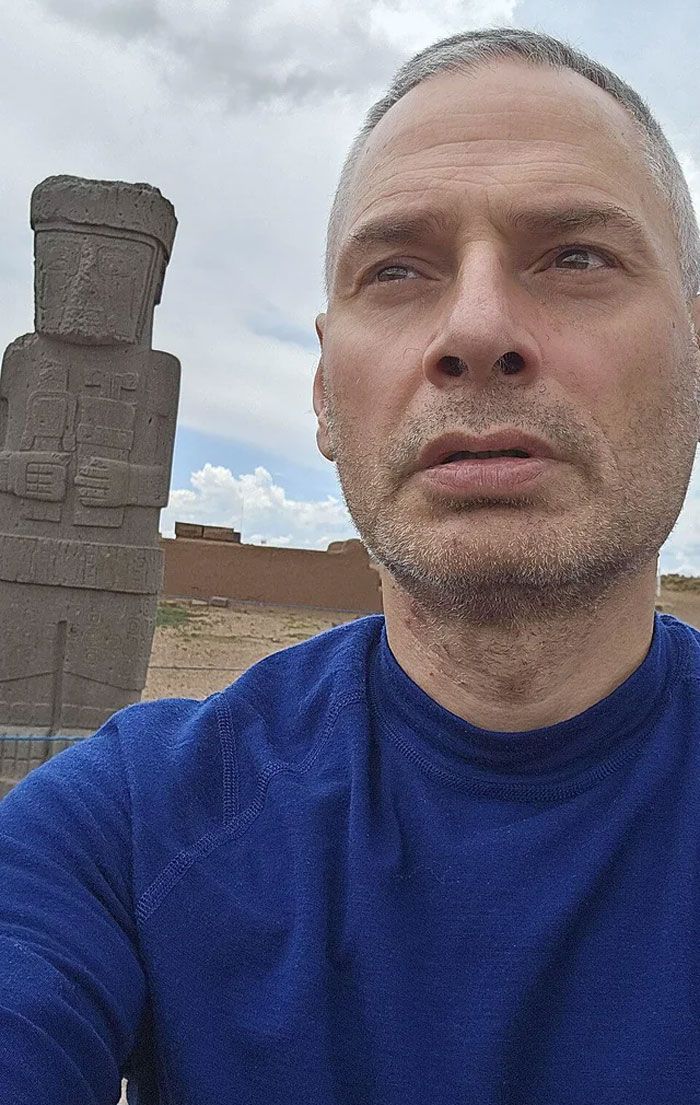 Middle-aged man in blue shirt near ancient stone statue, highlighting humans neurologically entering adulthood at age 32.