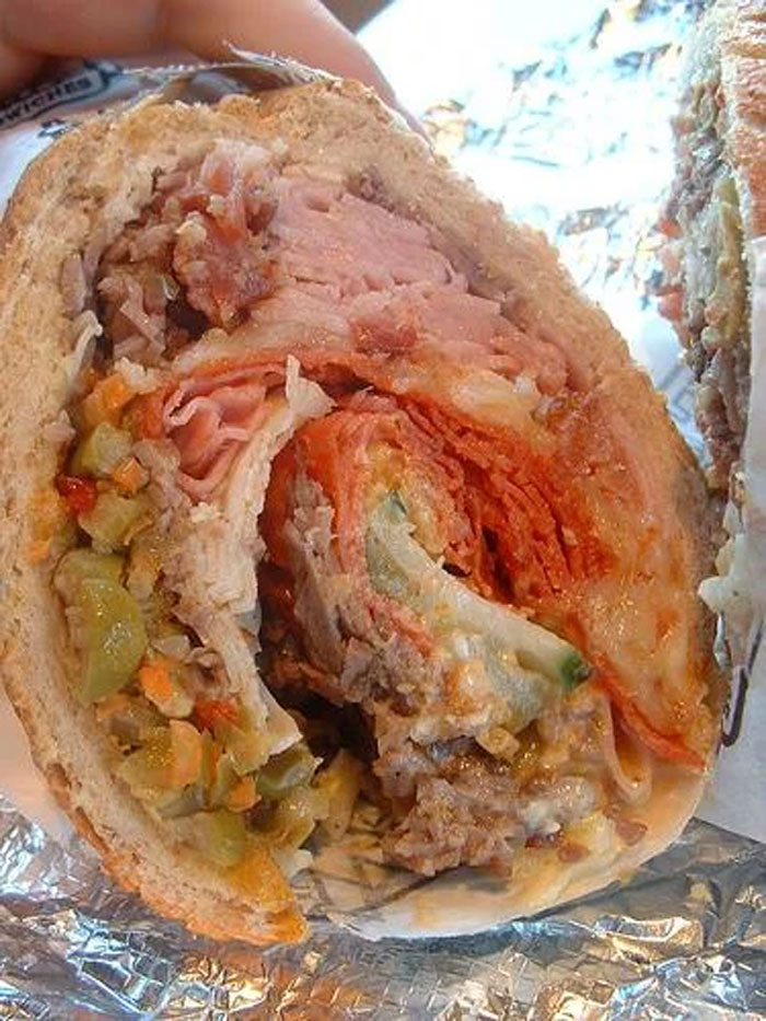 Close-up of a deli sub sandwich with layers of meat, cheese, and pickled vegetables on a hoagie roll.