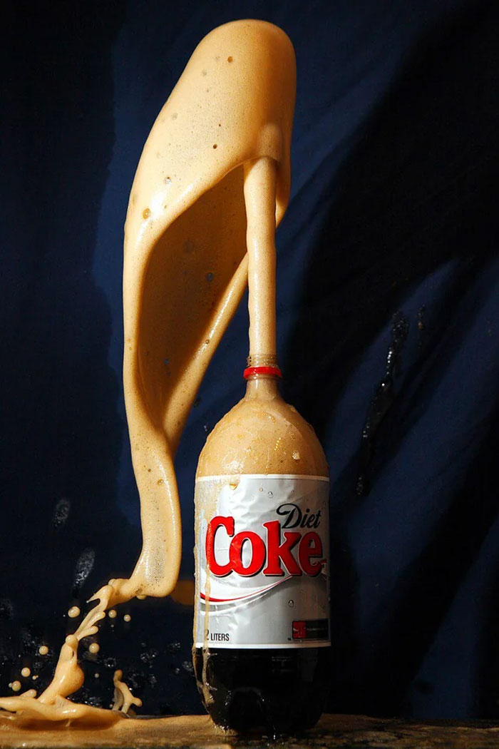 Diet Coke bottle with foam erupting against a dark background illustrating a chemical reaction and neurological maturity concept.