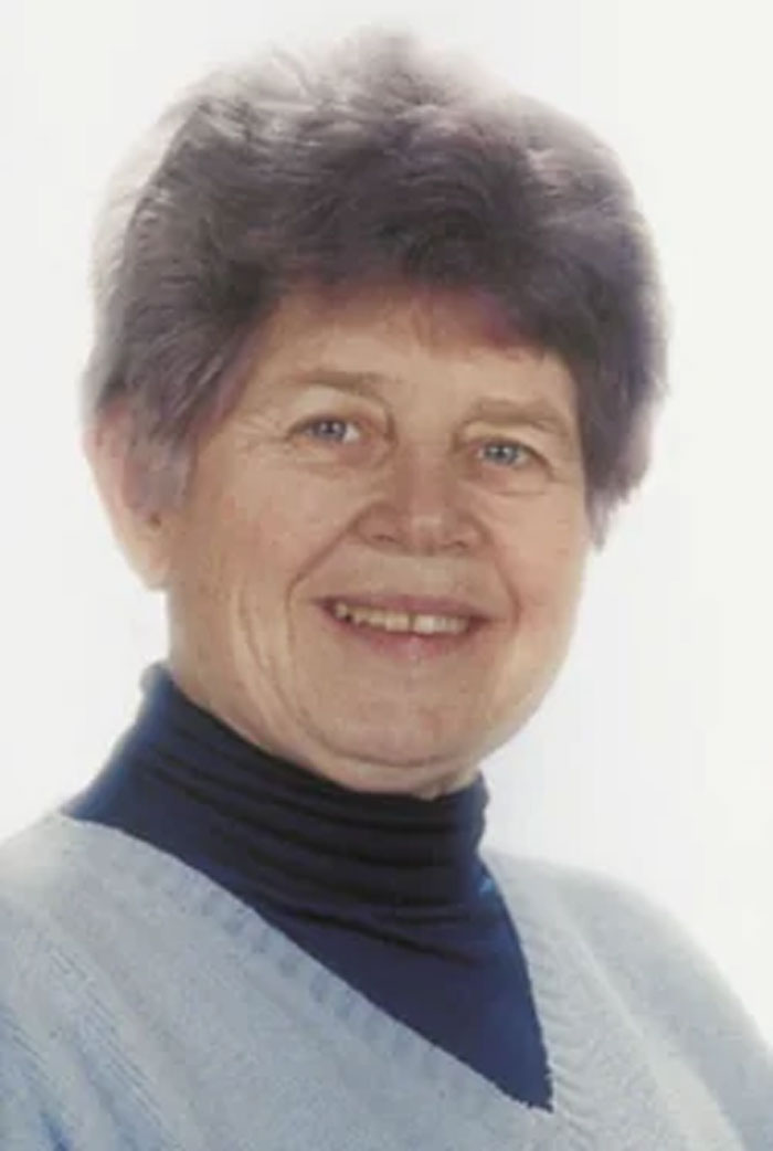 Smiling elderly woman with short gray hair, wearing a light sweater and dark turtleneck, symbolizing neurological adulthood.