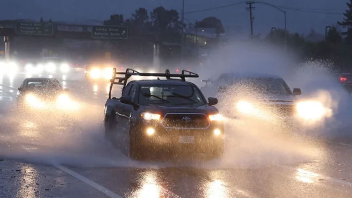 Cars driving through heavy rain and splashing water on a wet road during nighttime with headlights on.