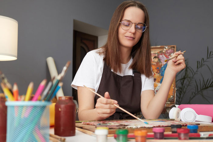 Woman painting at a desk surrounded by art supplies, illustrating the concept of trashing girlfriends gift creativity.