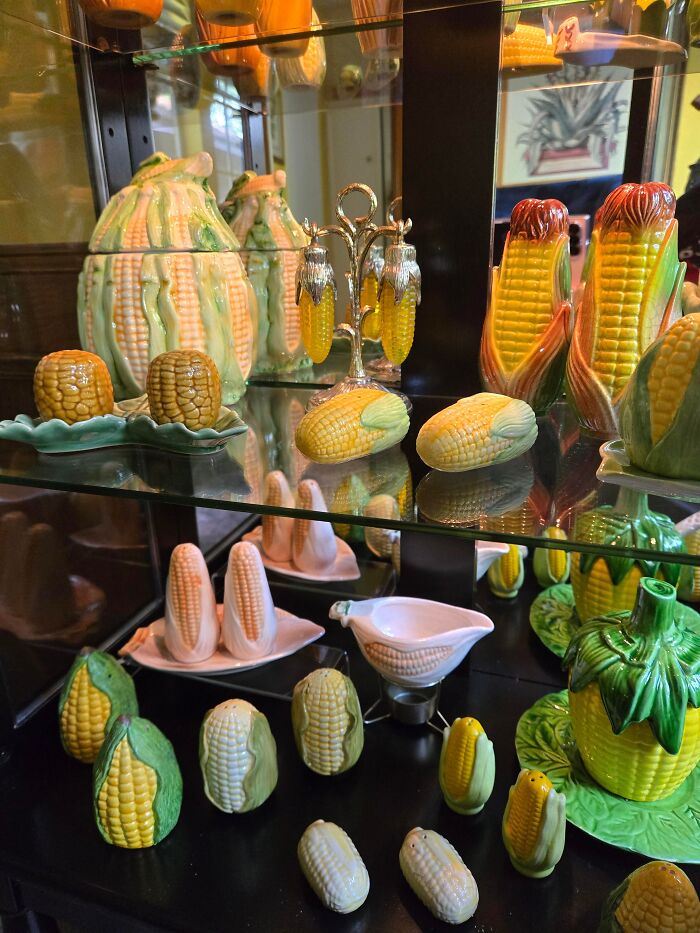 Collection of corn-themed ceramic items displayed on glass shelves, showcasing a unique and detailed obsession.