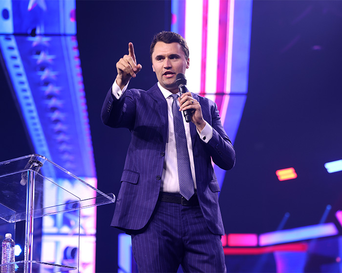 Turning Point USA college president speaking on stage in a suit during a public event before forced resignation controversy.