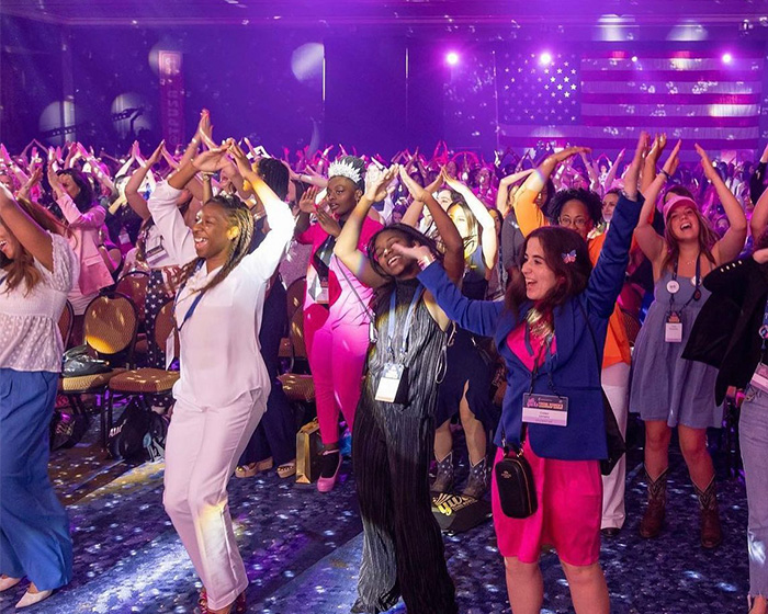 People dancing and celebrating at a Turning Point USA college event under purple stage lighting with an American flag backdrop.
