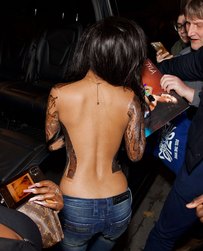 Tyla signing autographs wearing a bizarre adhesive top with snake print sleeves at Paris Fashion Week event.