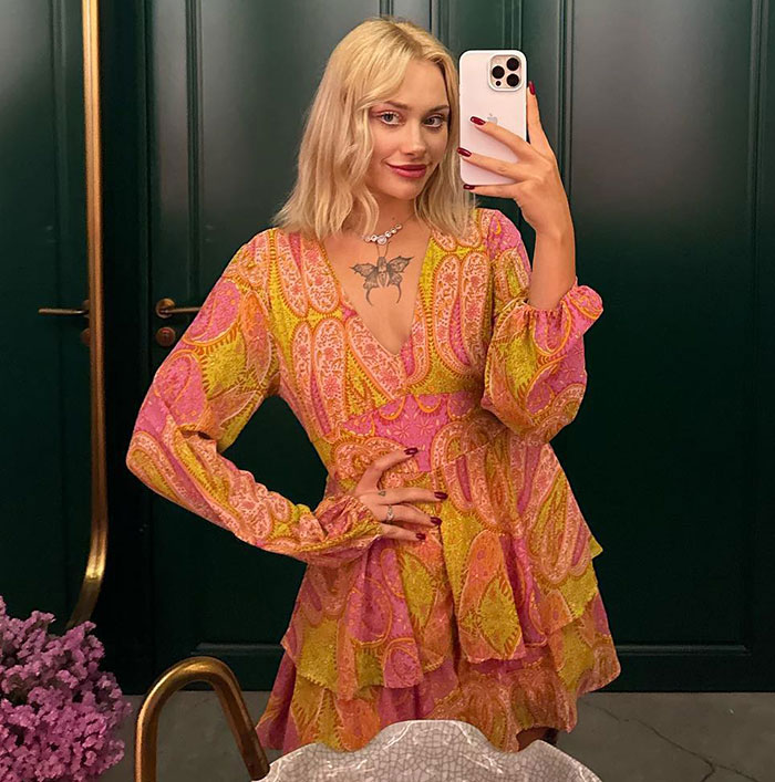 Model with horrific injuries poses for pics during comeback, wearing a colorful patterned dress and taking a mirror selfie indoors.