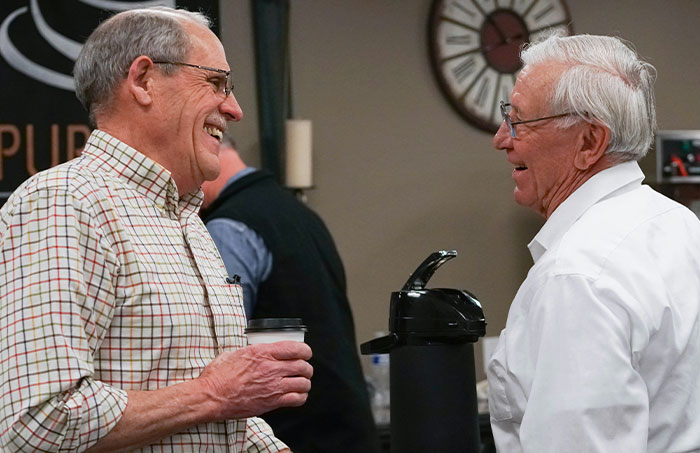 Two elderly men smiling and chatting over coffee, illustrating one-in-a-million stories that people actually lived through.