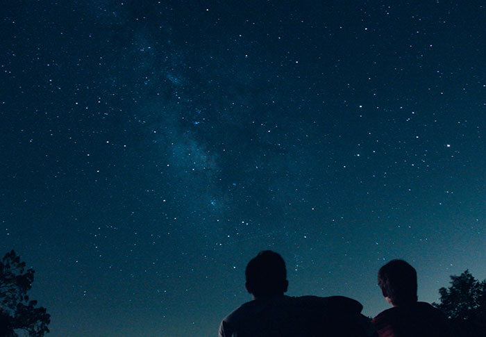 Two people stargazing under a clear night sky filled with stars, reflecting on one-in-a-million stories.