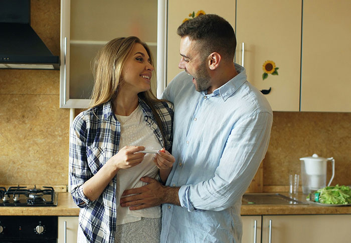 Couple in kitchen celebrating with a pregnancy test showing positive, a one-in-a-million story of real life moments.