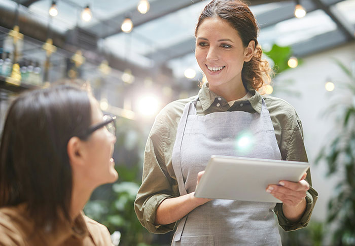 Young woman sharing one-in-a-million stories with a customer in a bright cafe setting, holding a tablet and smiling.