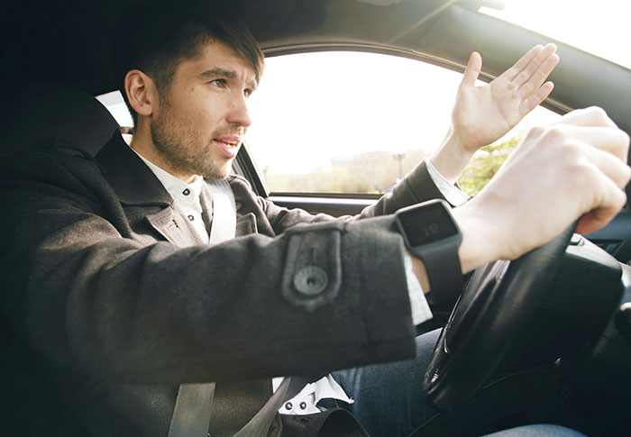 A man in a coat driving a car with an expressive gesture, illustrating one-in-a-million stories people lived through.
