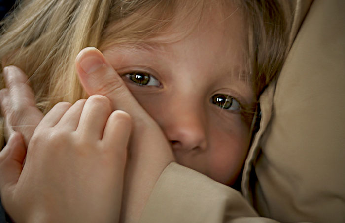 Close-up of a child’s face peeking from behind a hand, illustrating one-in-a-million stories people lived through.