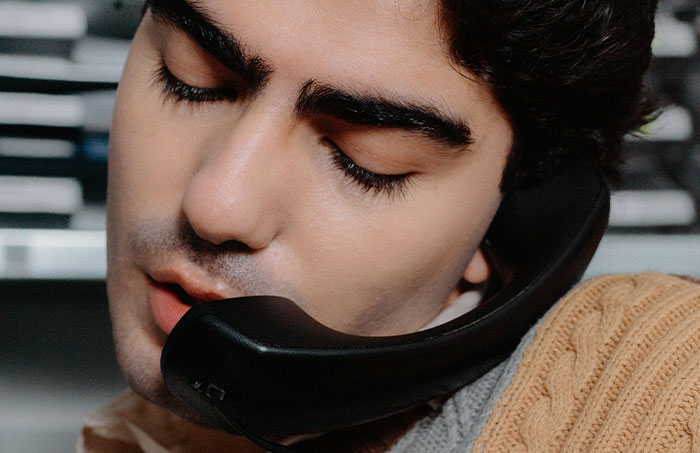 Young man holding a phone between head and shoulder, listening closely during a one-in-a-million story call.