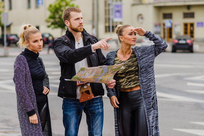 Three people navigating a city street using a map, illustrating unconventional family traditions outdoors.