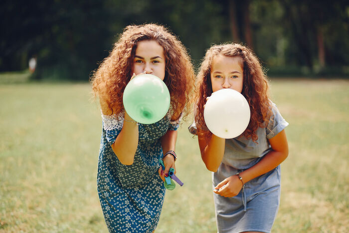 Two girls outdoors blowing up balloons, capturing unconventional family traditions in a heartwarming moment.