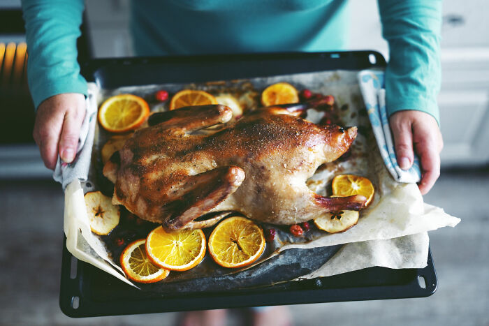Person holding a tray with a roasted duck surrounded by citrus slices representing unconventional family traditions.