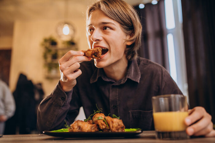 Young man enjoying a meal, representing unconventional family traditions involving food and shared moments at the table.