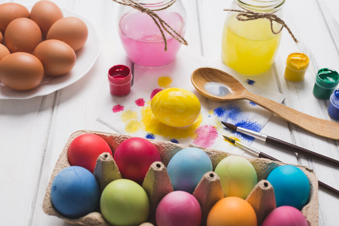 Colorful painted eggs and natural eggs on a table with paintbrushes and jars, depicting unconventional family traditions.