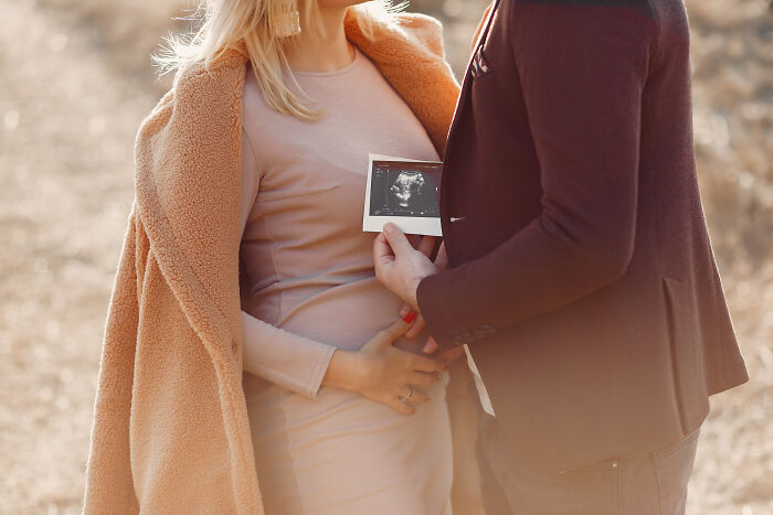 Couple sharing a tender moment holding an ultrasound photo, showcasing unconventional family traditions outdoors.