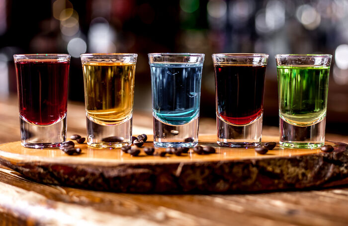 Five colorful shot glasses arranged on a wooden board, illustrating unconventional family traditions and celebrations.