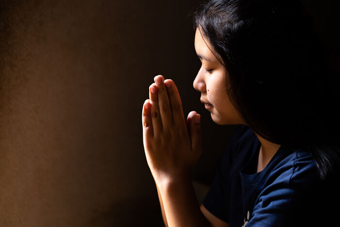 Young woman praying in dim light, reflecting on unconventional family traditions and personal moments.