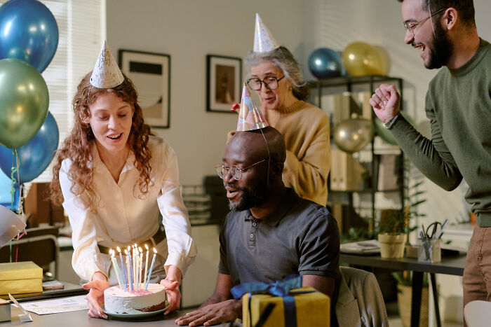 Group of friends wearing party hats celebrating with cake and gifts, showcasing unconventional family traditions.