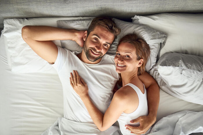 Smiling couple lying in bed together, sharing a warm moment reflecting unconventional family traditions.