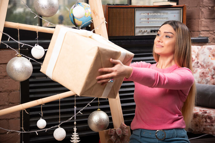 Woman in pink sweater holding a wrapped gift near unconventional family traditions holiday decorations.