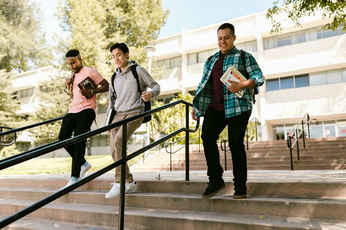 Three diverse students walking down school steps outdoors, reflecting on challenging beliefs and controversial opinions.