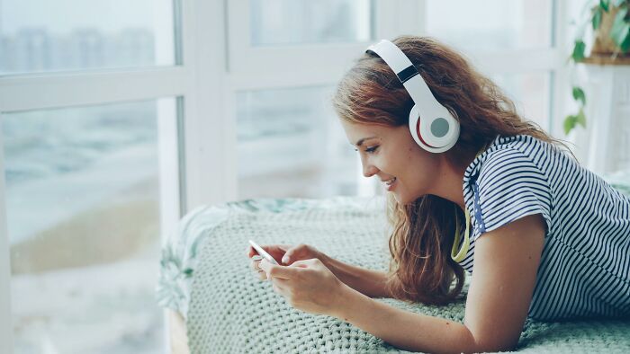 Young woman wearing headphones and smiling while using a smartphone, engaging in challenge your beliefs content.
